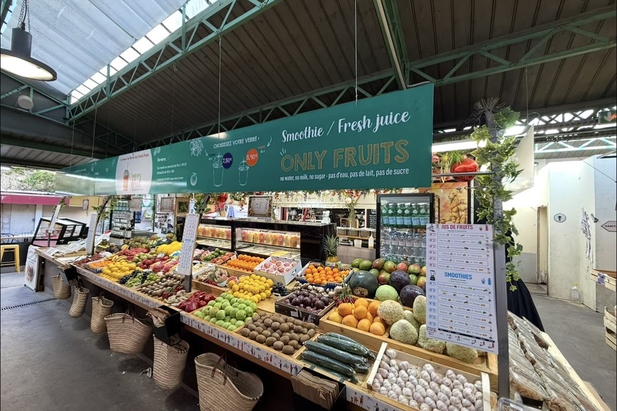 A fruit and juice stall inside the Marché des Enfants Rouges, crates of produce under a green Only Fruits banner